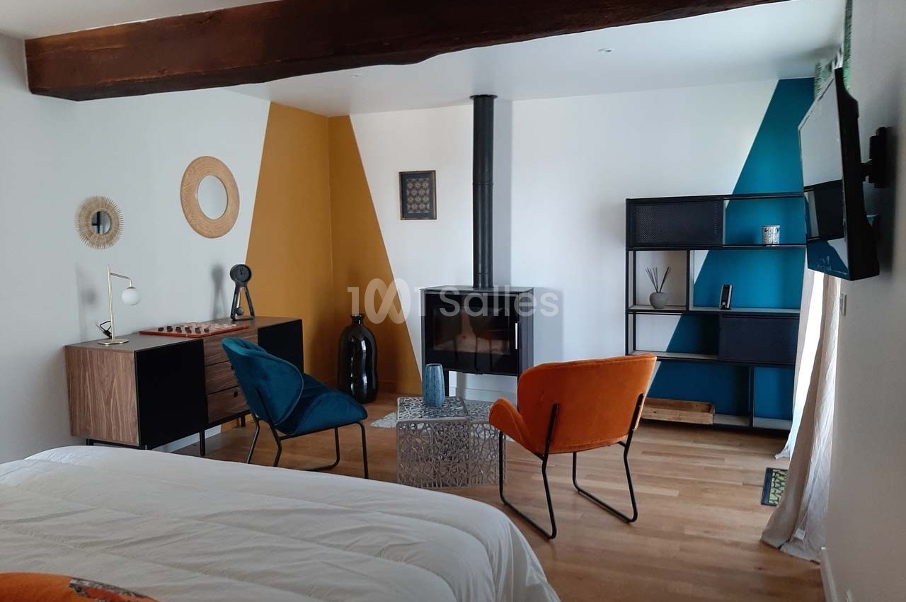 Chambre moderne avec lit, poêle à bois, fauteuils colorés, étagère et murs aux motifs géométriques.