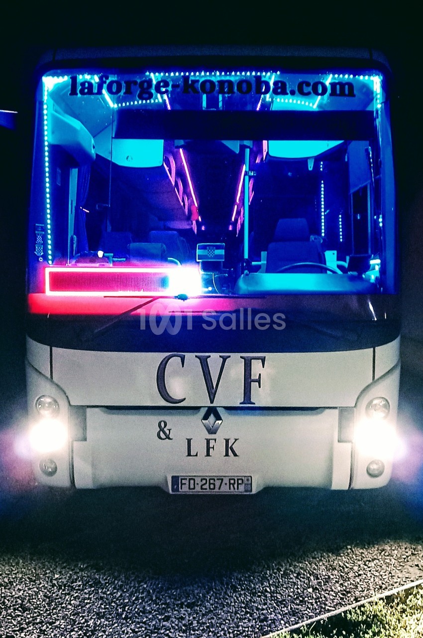 Autobus illuminé par des néons colorés, stationné de nuit avec une enseigne visible sur le pare-brise.