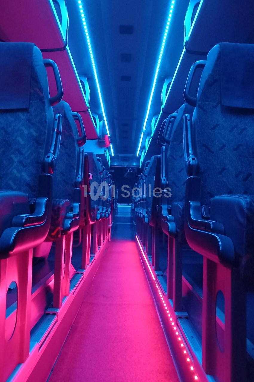 Allée centrale d'un bus vide avec éclairage intérieur bleu et rose, sièges alignés de chaque côté.