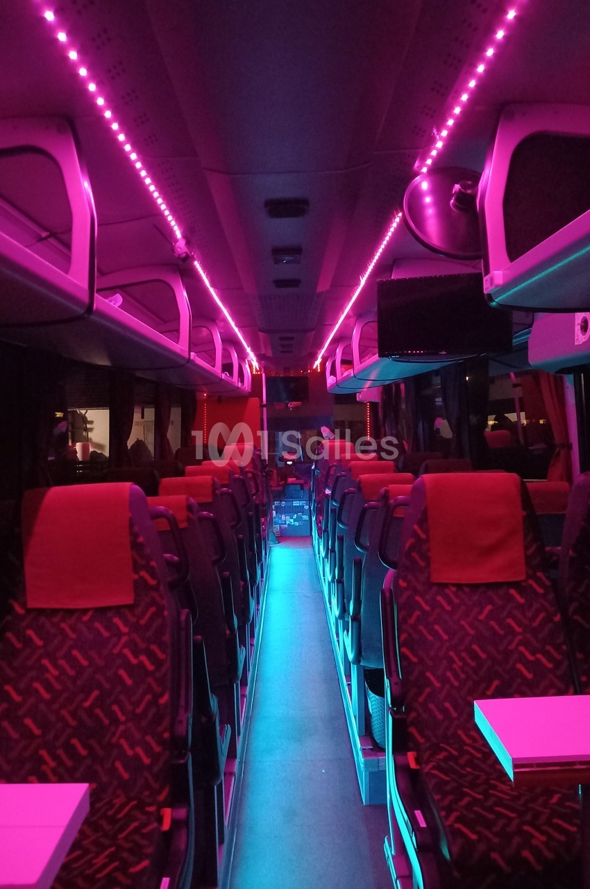 Intérieur d'un bus avec éclairage LED rose et bleu, rangées de sièges vides et tablettes rabattables.