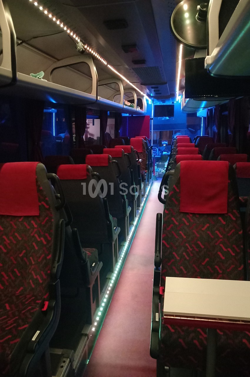 Intérieur d'un autocar vide avec sièges rouges et noirs, éclairage tamisé et allée centrale illuminée.