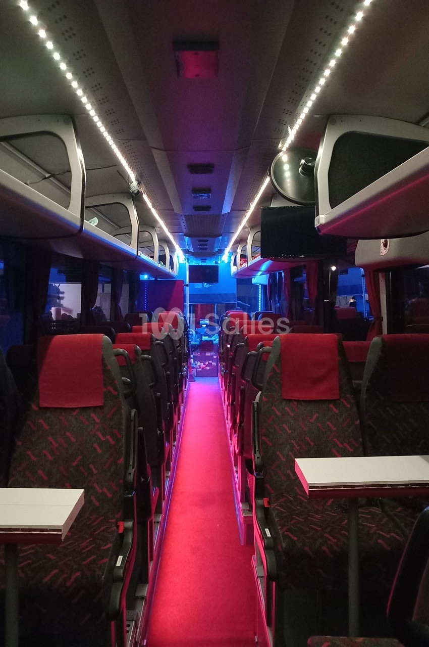 Intérieur d'un autocar avec sièges rouges, éclairage tamisé et allée centrale recouverte d'un tapis rouge.