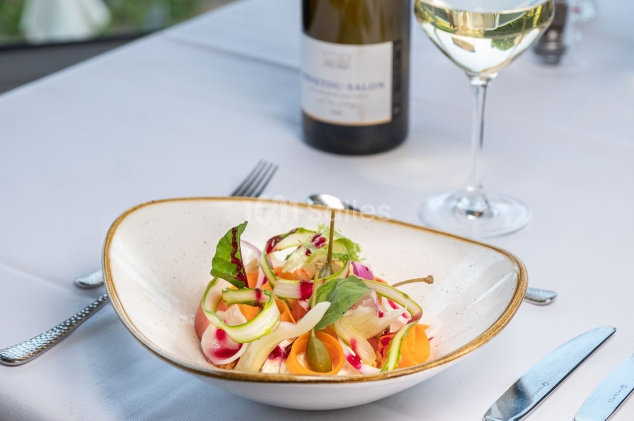Assiette de salade colorée avec légumes frais, servie sur une table dressée avec verre de vin blanc et bouteille.
