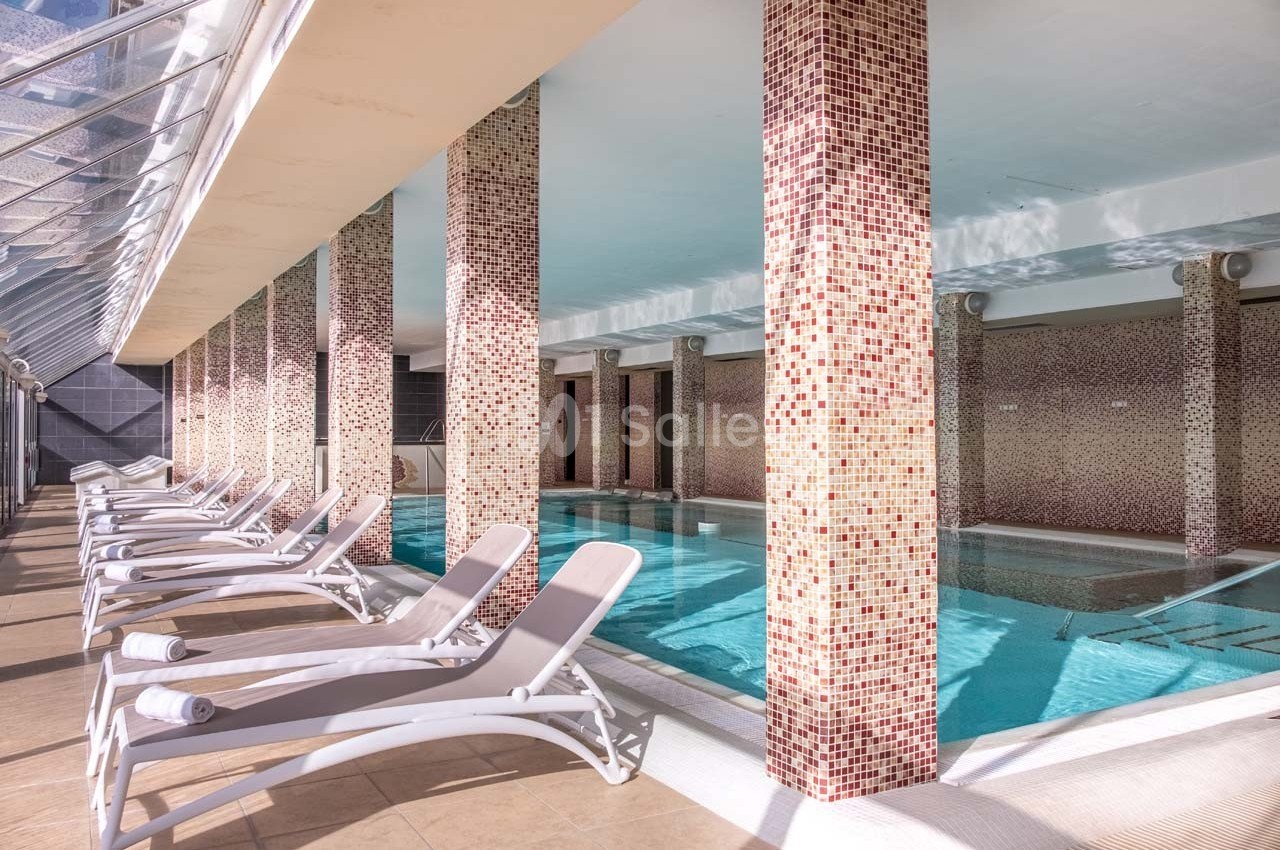 Piscine intérieure avec colonnes décoratives et transats alignés le long d'un sol carrelé clair.