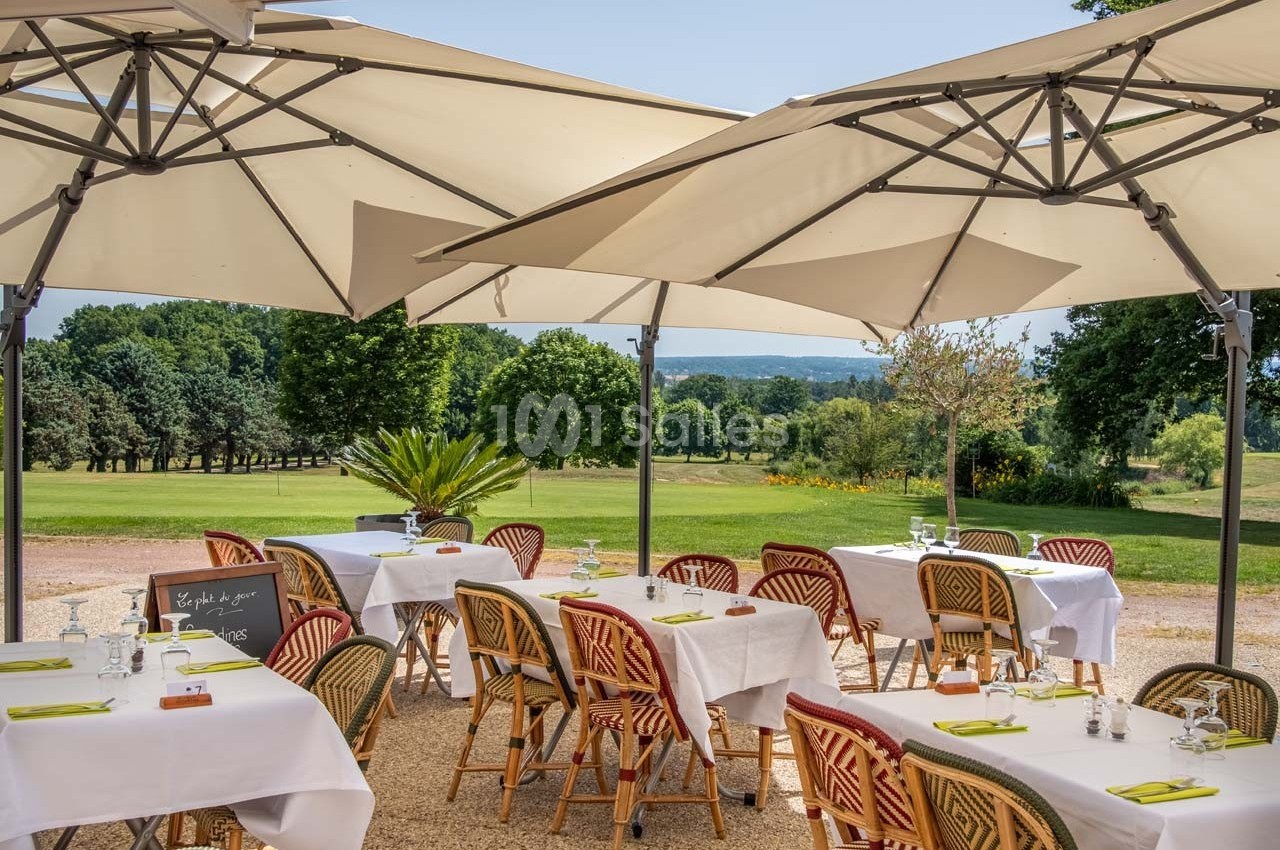 Terrasse d'un restaurant avec tables dressées sous des parasols, offrant une vue sur un paysage verdoyant.