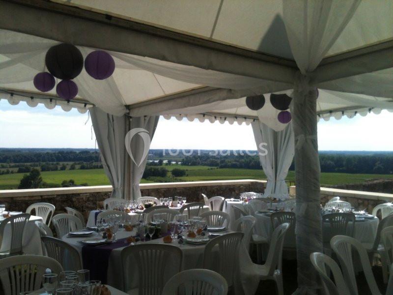 Tente blanche décorée de ballons violets, abritant des tables dressées avec vue sur un paysage verdoyant.