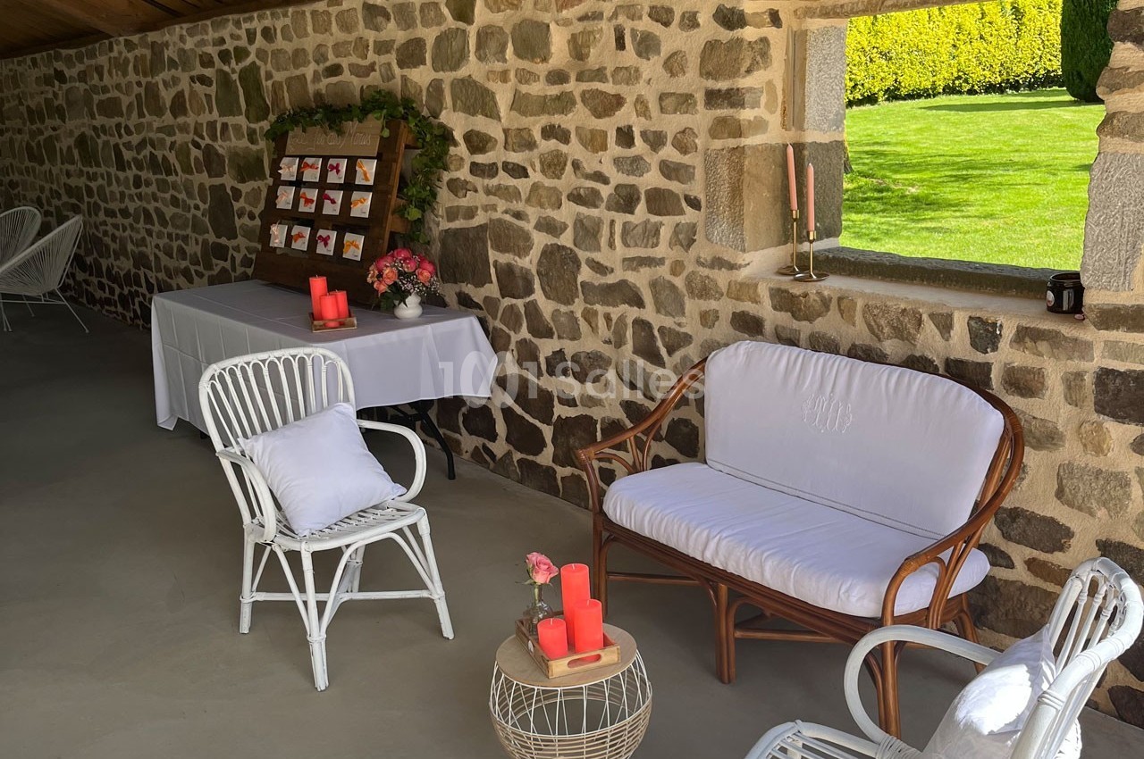 Espace extérieur aménagé avec des meubles en rotin, une table décorée et un présentoir sur un mur en pierre.