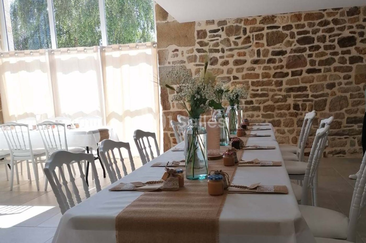 Salle lumineuse avec tables décorées de nappes blanches, chemins de table en toile de jute et bouquets de fleurs.