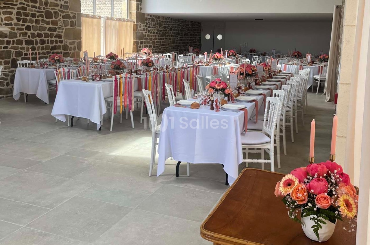 Salle décorée pour un événement avec des tables dressées, des nappes blanches et des bouquets de fleurs colorées.
