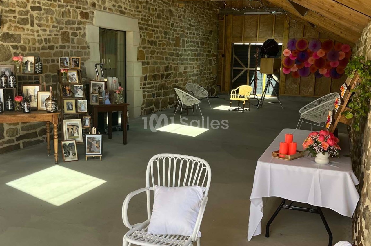 Salle en pierre décorée avec des cadres photo, des chaises blanches et des bougies sur une table.