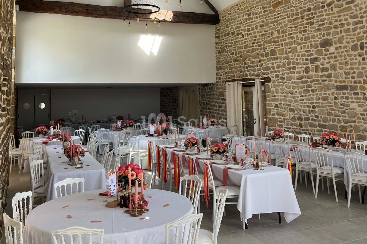 Salle de réception décorée pour un événement, avec tables dressées, nappes blanches et compositions florales colorées.
