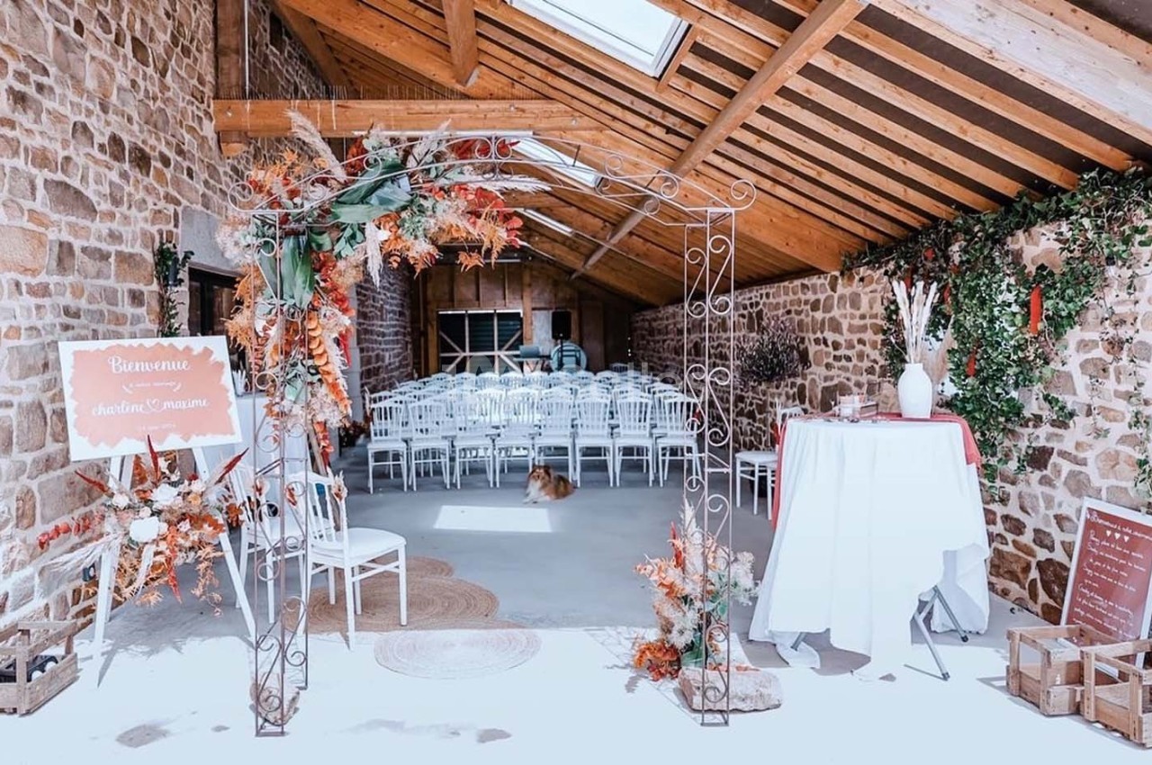 Salle de réception rustique avec des chaises blanches alignées, une arche décorée et des murs en pierre apparente.