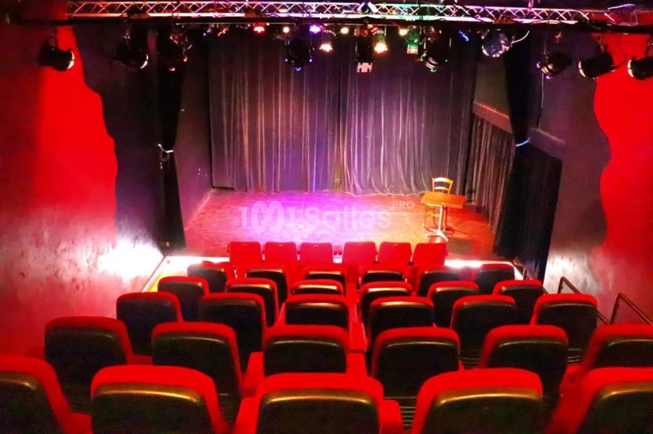 Salle de spectacle avec rangées de sièges rouges, scène éclairée et rideaux noirs en arrière-plan.