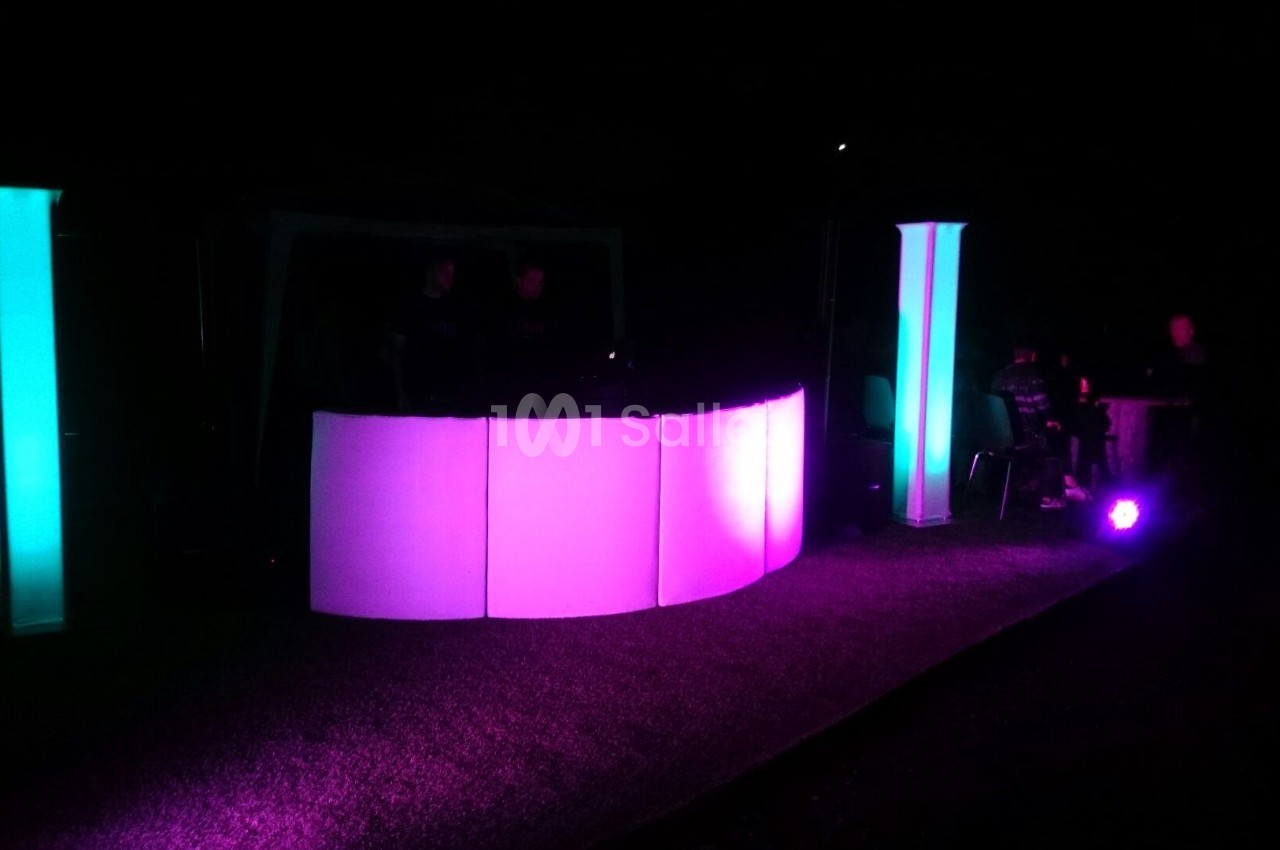 Installation lumineuse avec des colonnes et un comptoir éclairés en rose et bleu dans un environnement sombre.