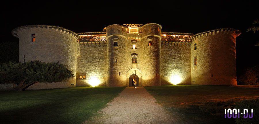 Façade d'un château en pierre éclairée la nuit, avec une entrée voûtée et des tours rondes.
