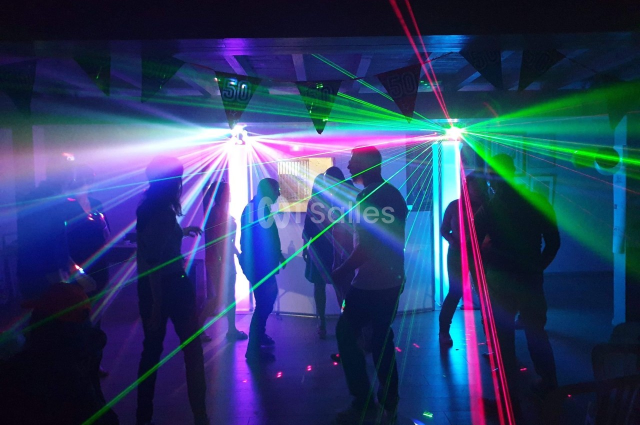 Personnes dansant dans une salle sombre illuminée par des faisceaux lumineux colorés et des lasers.
