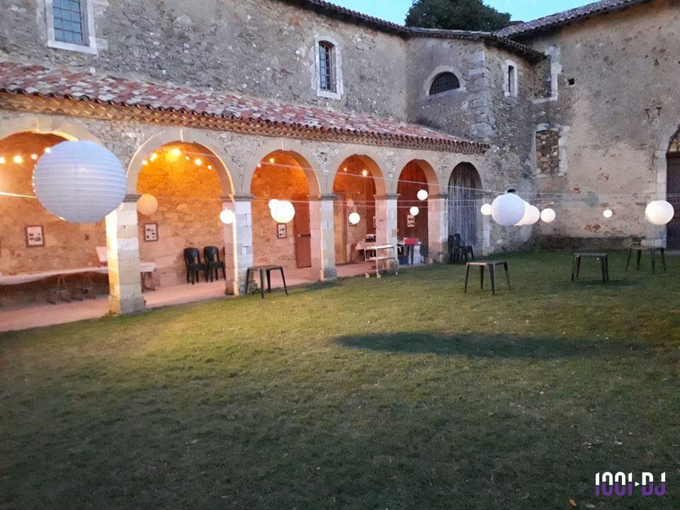 Cour intérieure d'un bâtiment ancien avec des arches éclairées et des lanternes suspendues au-dessus d'une pelouse.