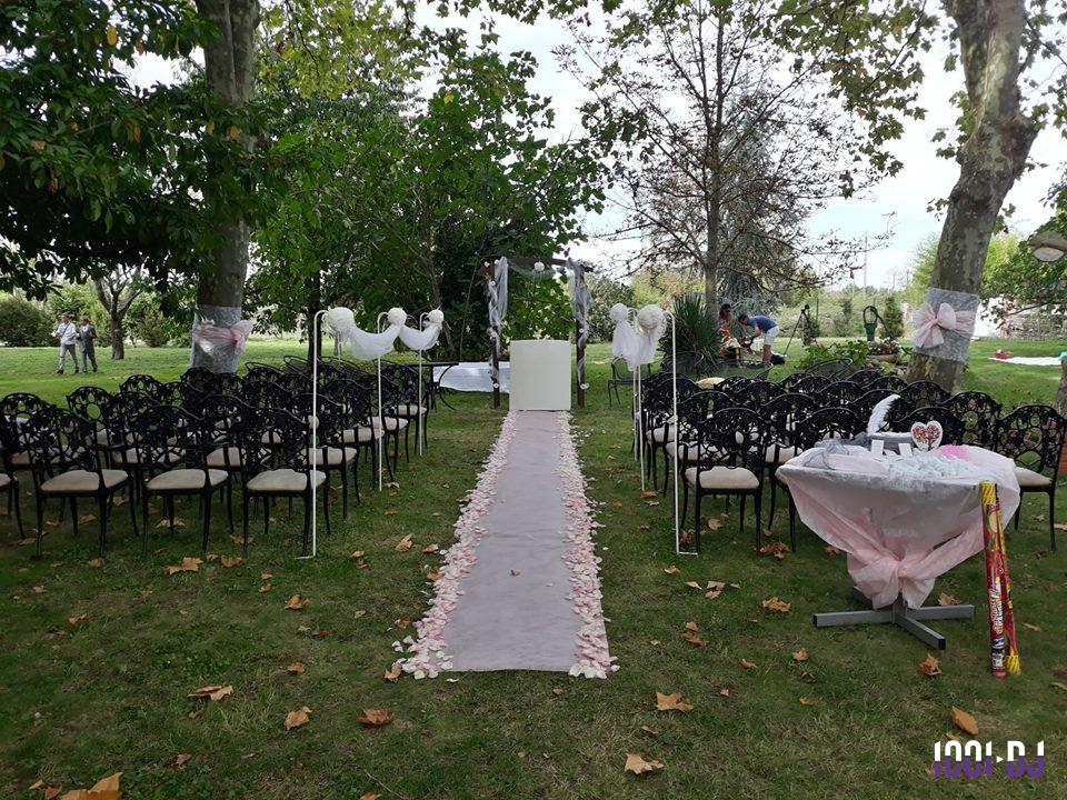Allée décorée de pétales de rose menant à une arche pour une cérémonie en plein air, entourée de chaises noires.