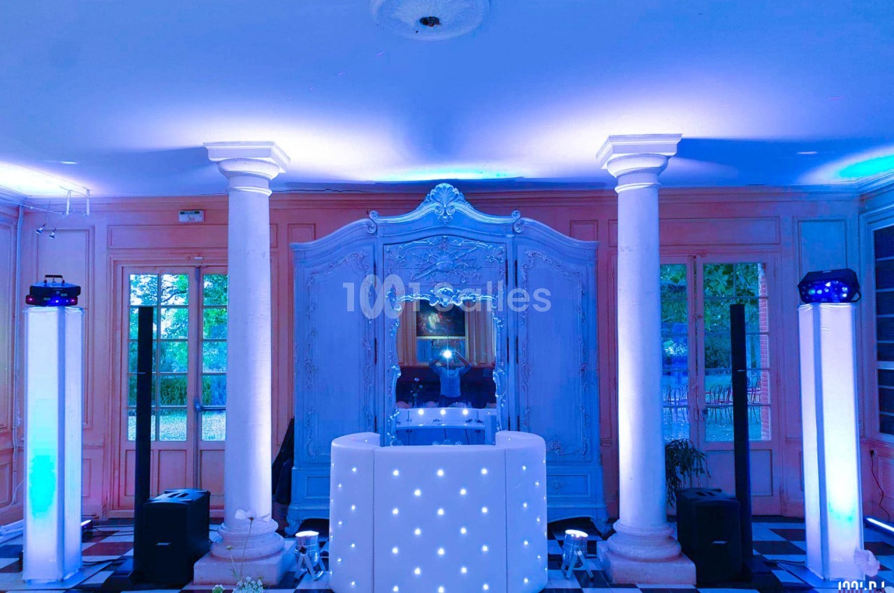 Salle élégante avec colonnes, éclairage bleu, mobilier lumineux et miroir orné au centre.