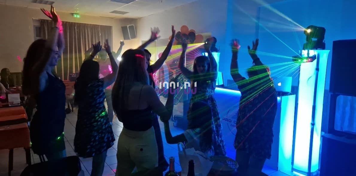Des personnes dansent dans une salle éclairée par des lumières colorées et des lasers près d'une table de DJ.