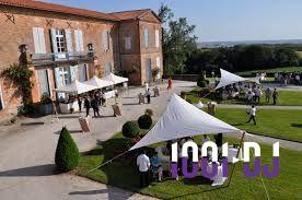 Des invités rassemblés sous des tentes blanches dans le jardin d'un grand bâtiment en briques rouges.