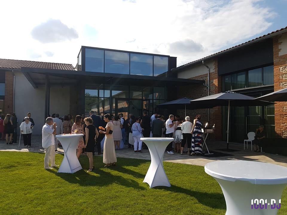 Groupe de personnes rassemblées devant un bâtiment moderne avec grandes baies vitrées, tables hautes et parasols.