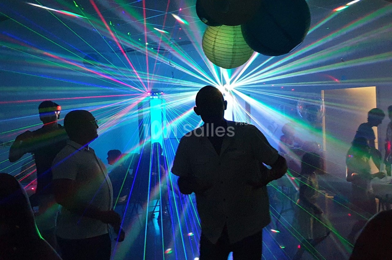 Personnes dansant dans une salle sombre illuminée par des faisceaux lumineux colorés et des décorations suspendues.