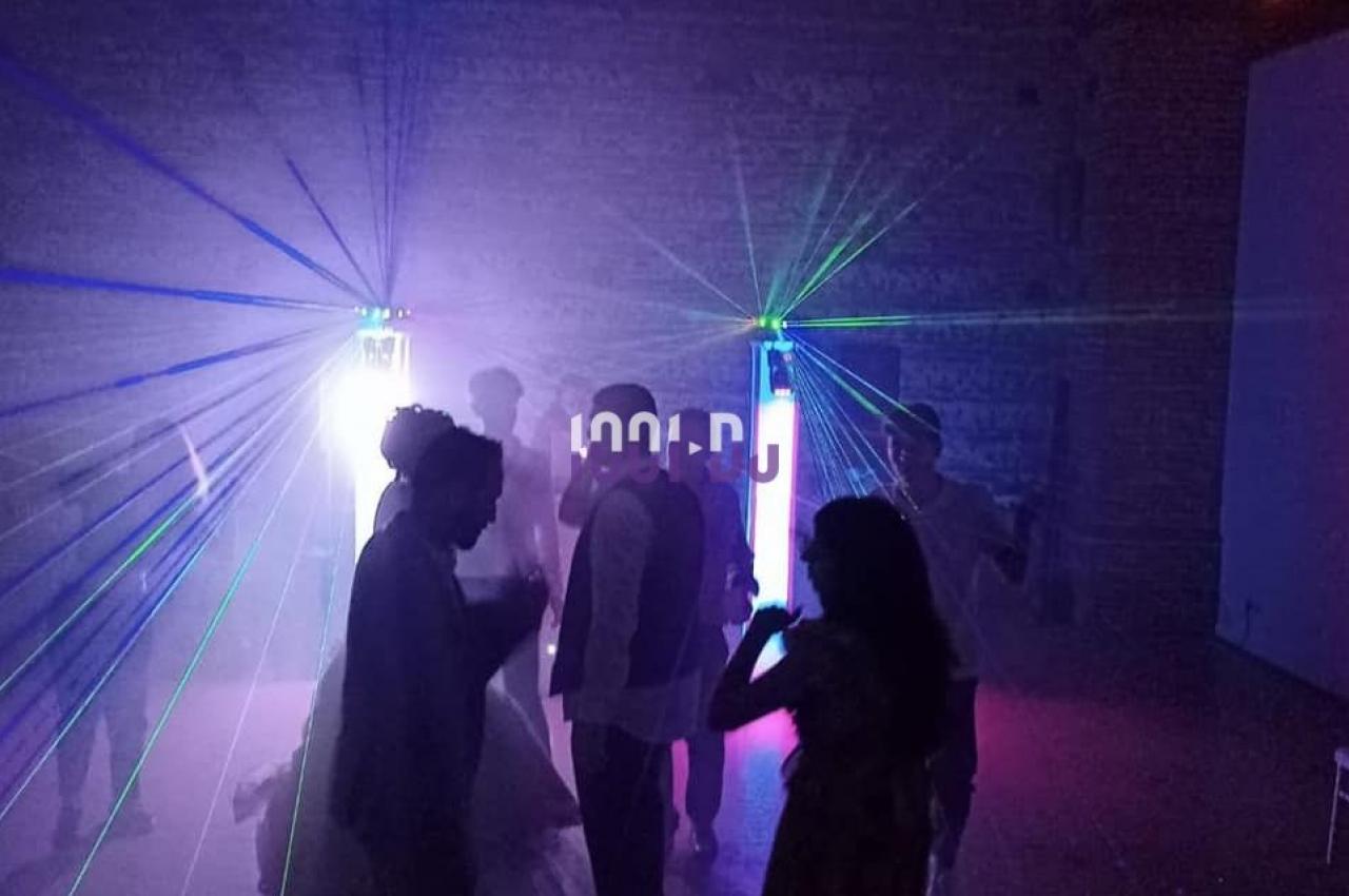 Des personnes dansent dans une salle sombre éclairée par des faisceaux lumineux colorés et des effets de fumée.