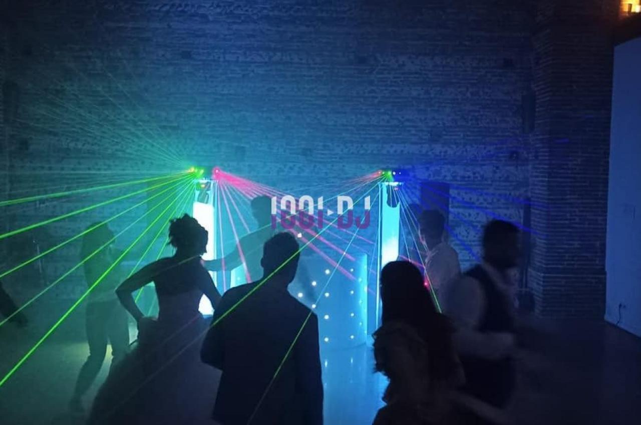 Des personnes dansent dans une salle sombre éclairée par des lasers colorés et des lumières de fête.