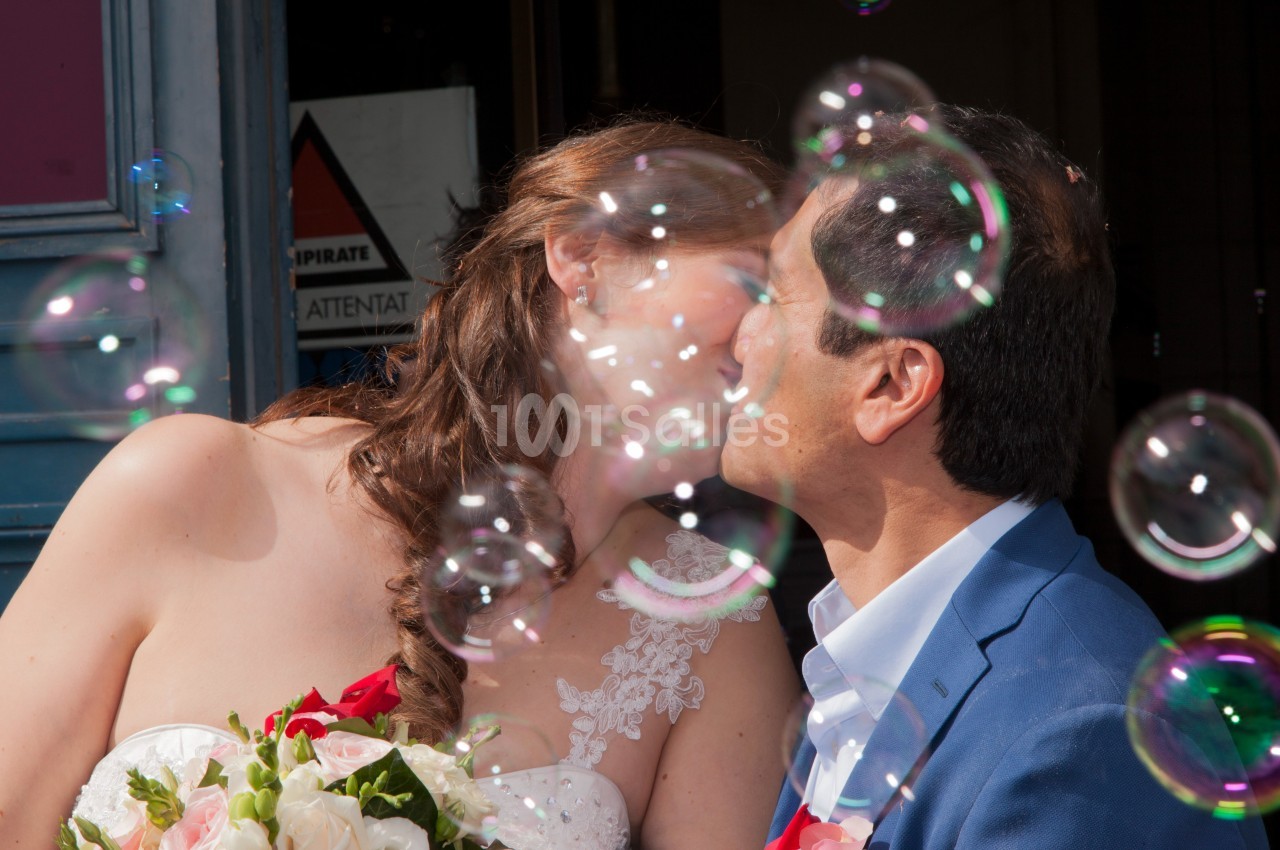 Un couple s'embrasse entouré de bulles de savon, la mariée tenant un bouquet de fleurs.