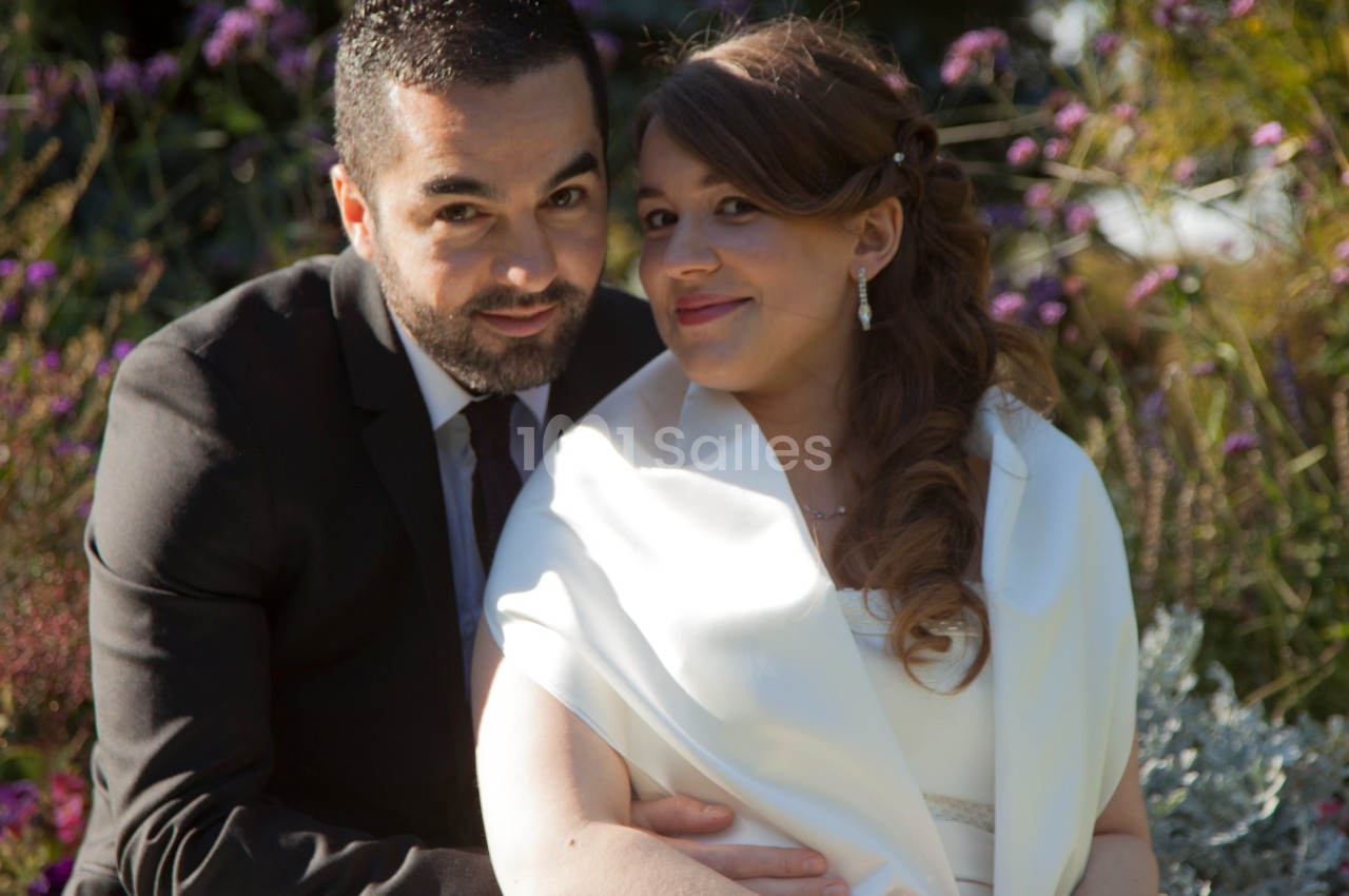 Un couple assis dans un jardin, habillé élégamment, souriant et entouré de végétation.