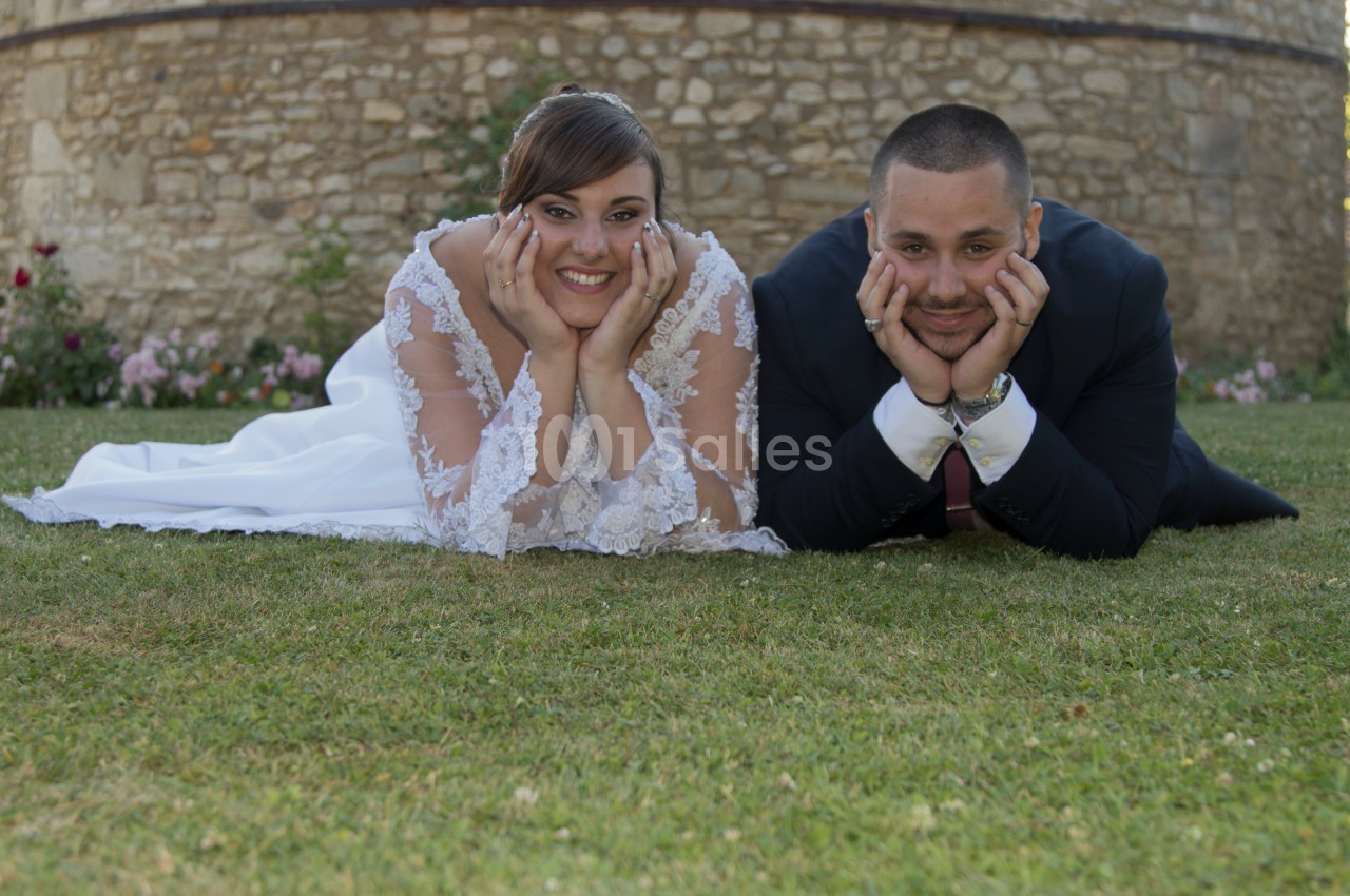 Un couple allongé sur l'herbe, souriant, devant un mur en pierre.