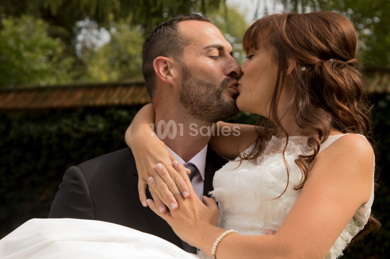Un couple en tenue de mariage s'embrasse tendrement dans un jardin verdoyant.