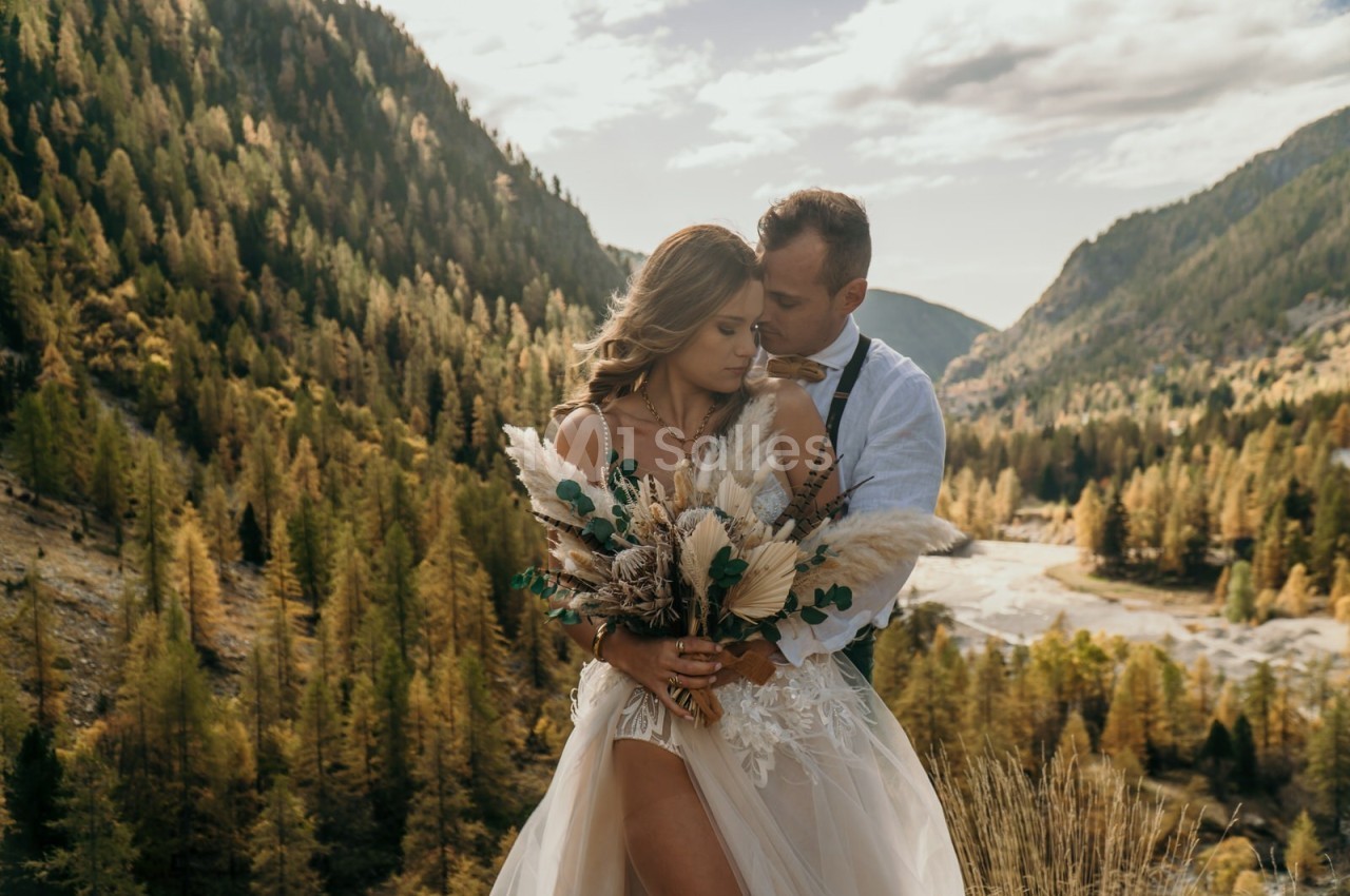 Un couple en tenue de mariage pose dans un paysage montagneux avec une forêt en arrière-plan.