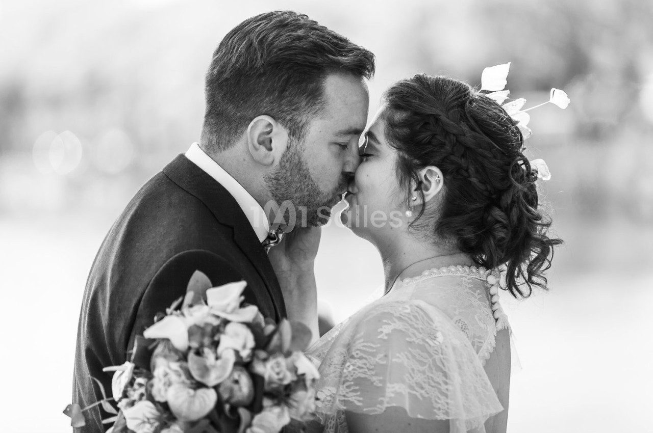 Un couple en tenue de mariage s'embrasse tendrement, la mariée tenant un bouquet de fleurs.