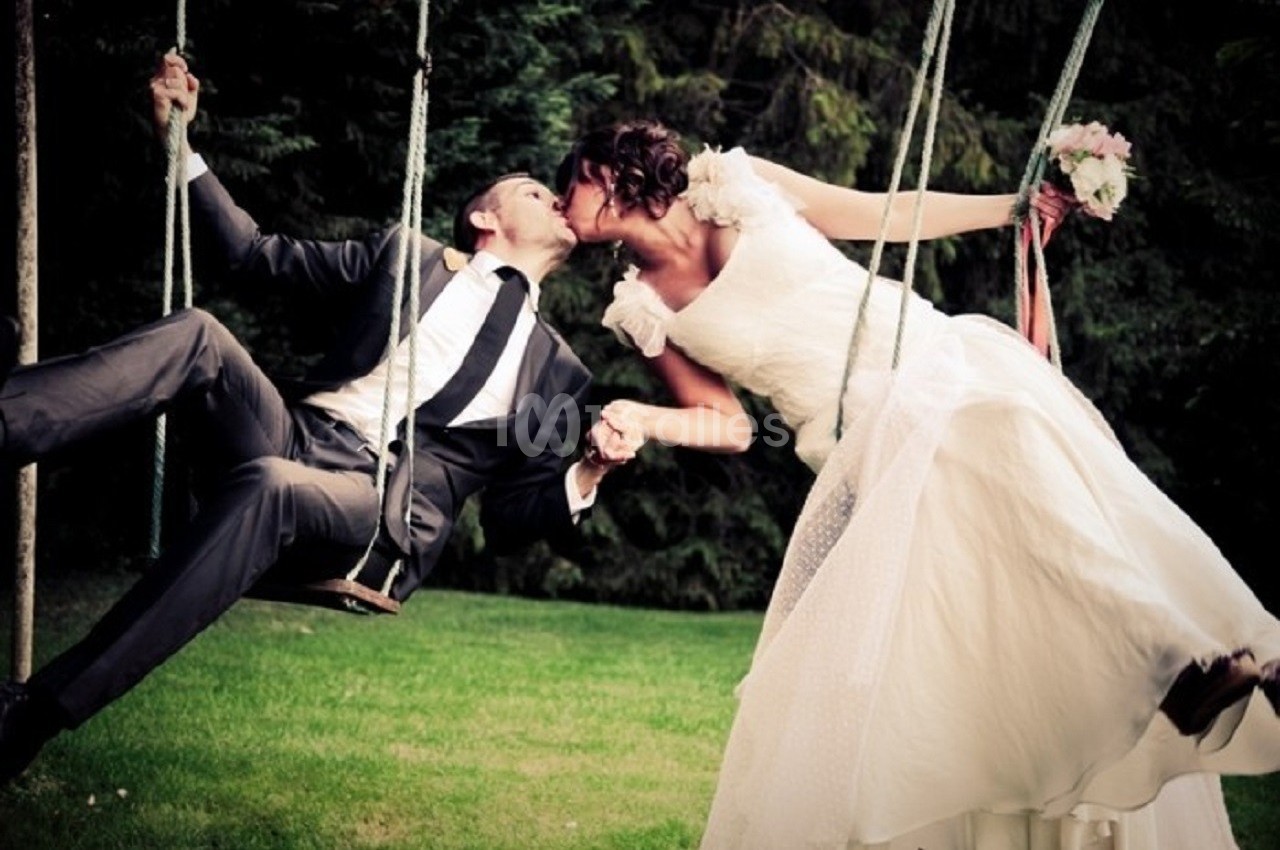 Un couple en tenue de mariage s'embrasse sur des balançoires dans un jardin verdoyant.