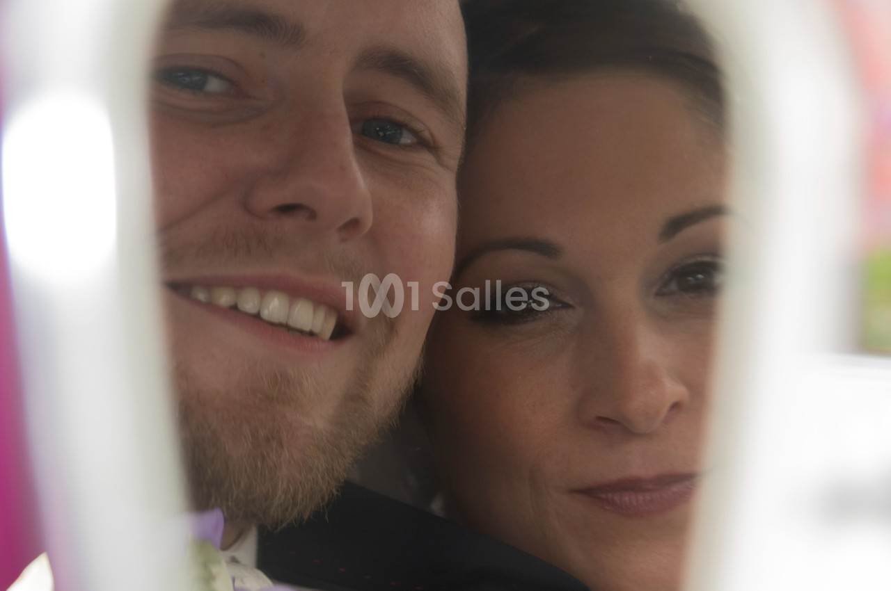 Un couple souriant photographié de près, partiellement encadré par un élément flou au premier plan.