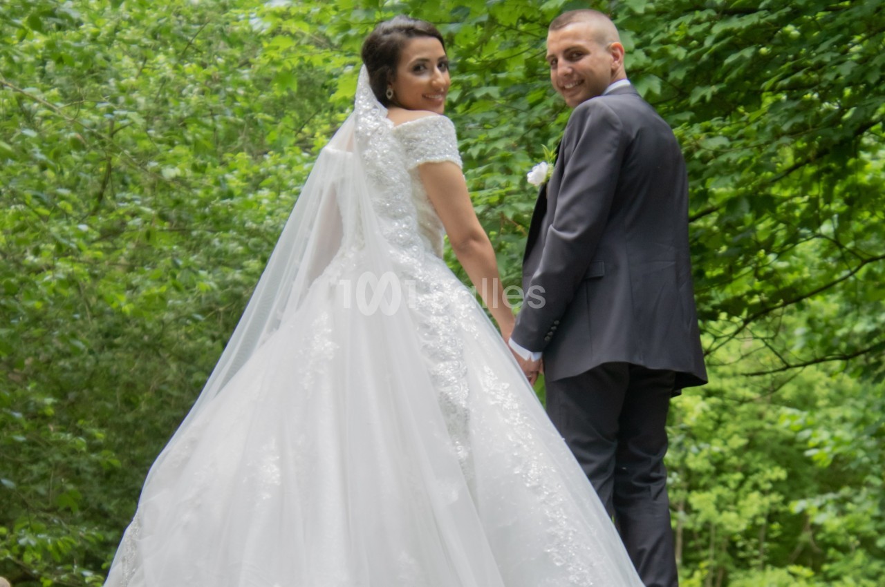 Un couple en tenue de mariage se tient dans un environnement verdoyant, regardant vers l'objectif.
