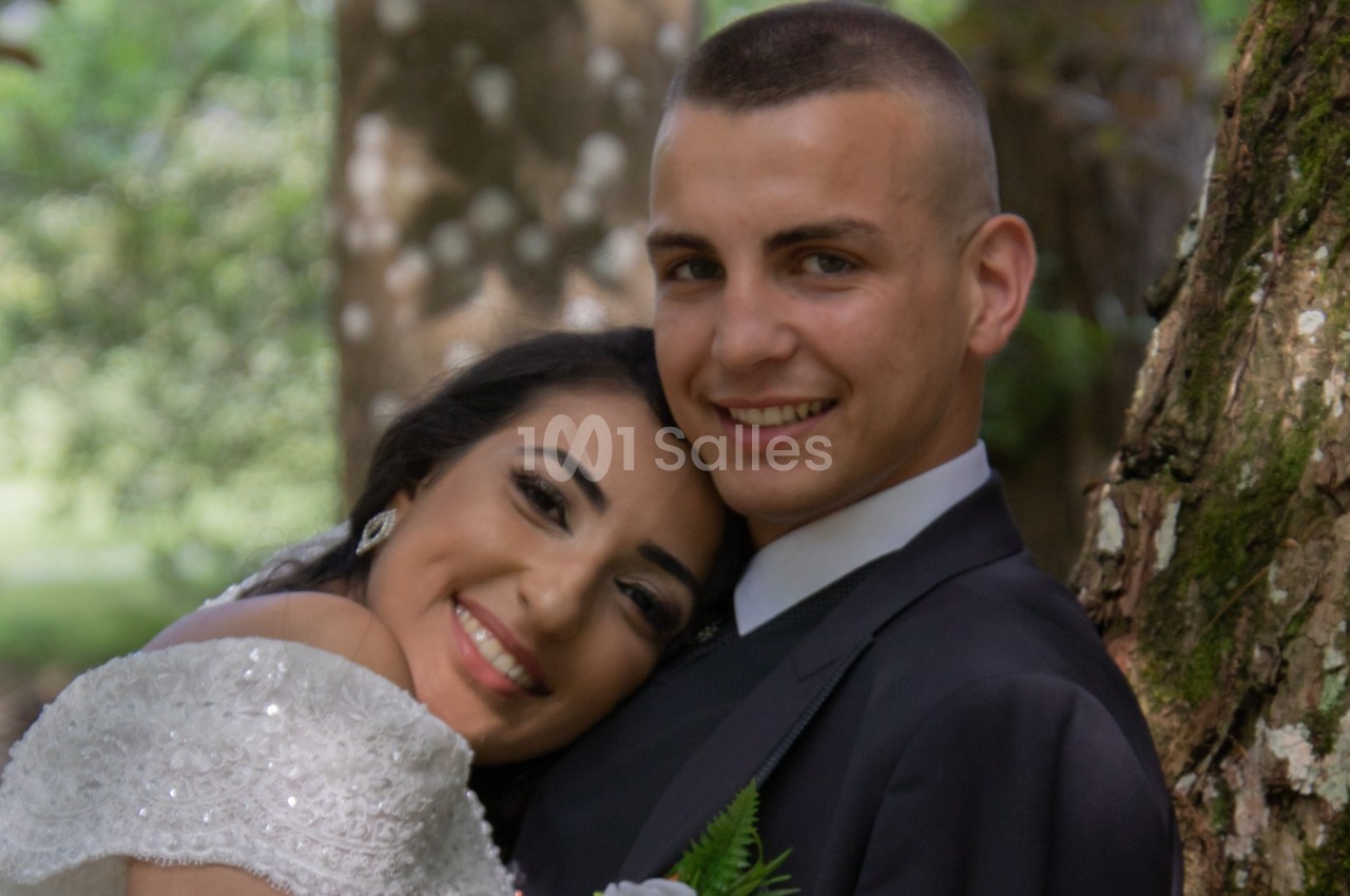 Un couple souriant, vêtu élégamment, pose près d'un arbre dans un cadre naturel.