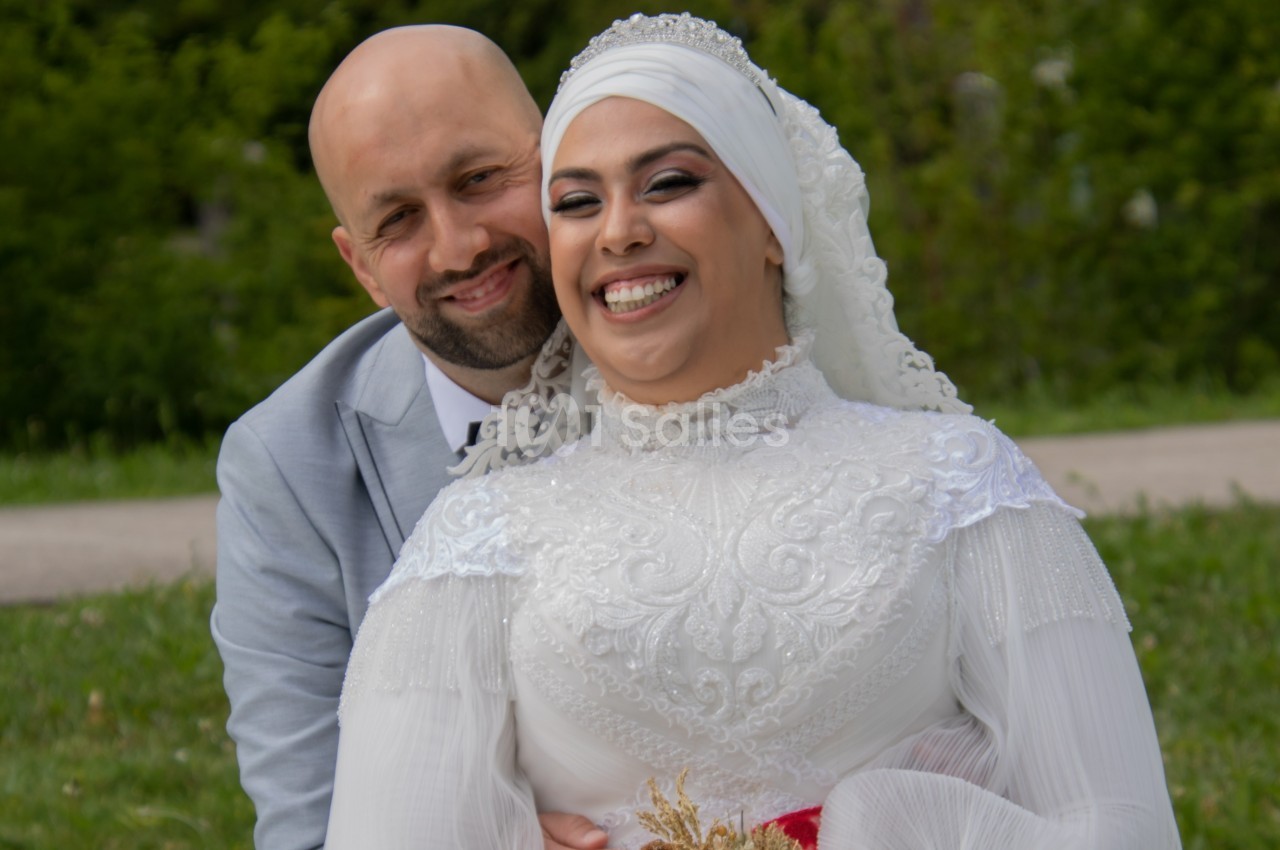 Un couple souriant en tenue de mariage, posant dans un parc verdoyant.