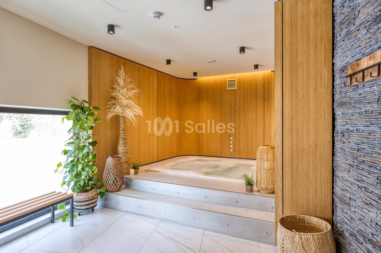 Bain à remous encastré dans une pièce lumineuse avec murs en bois, plantes et décorations naturelles.