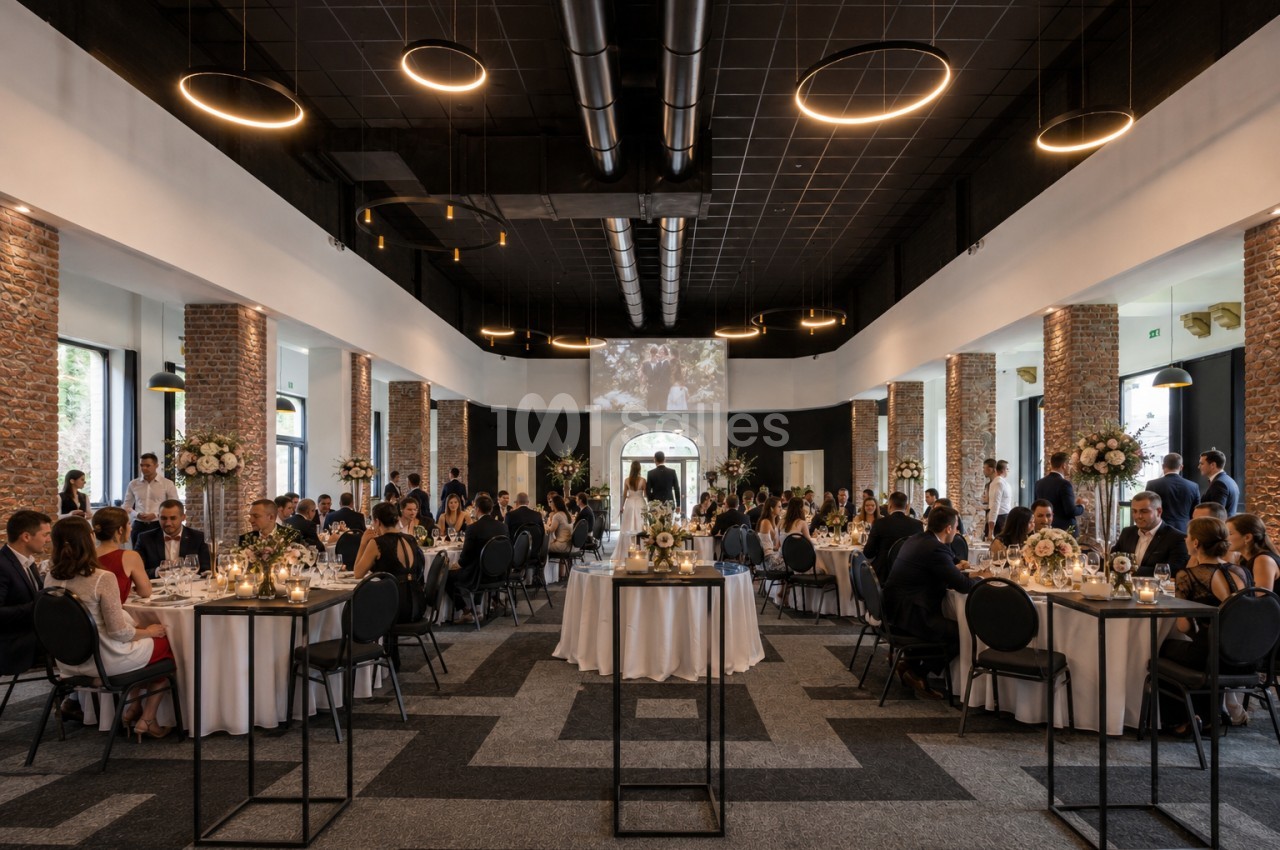 Salle de réception élégante avec invités assis à des tables décorées, éclairée par des luminaires modernes.