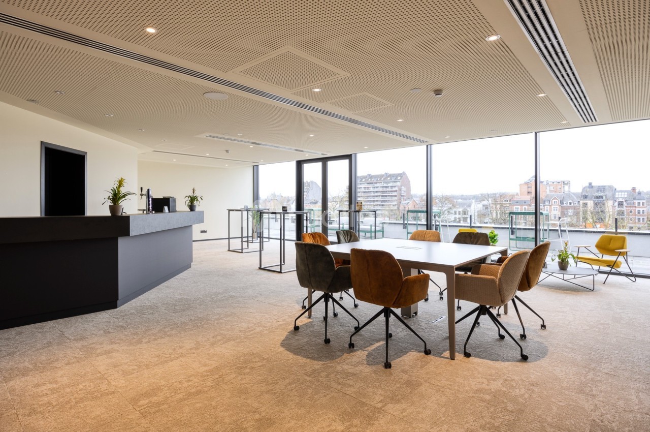 Salle de réunion lumineuse avec table, chaises colorées et grandes baies vitrées donnant sur un paysage urbain.