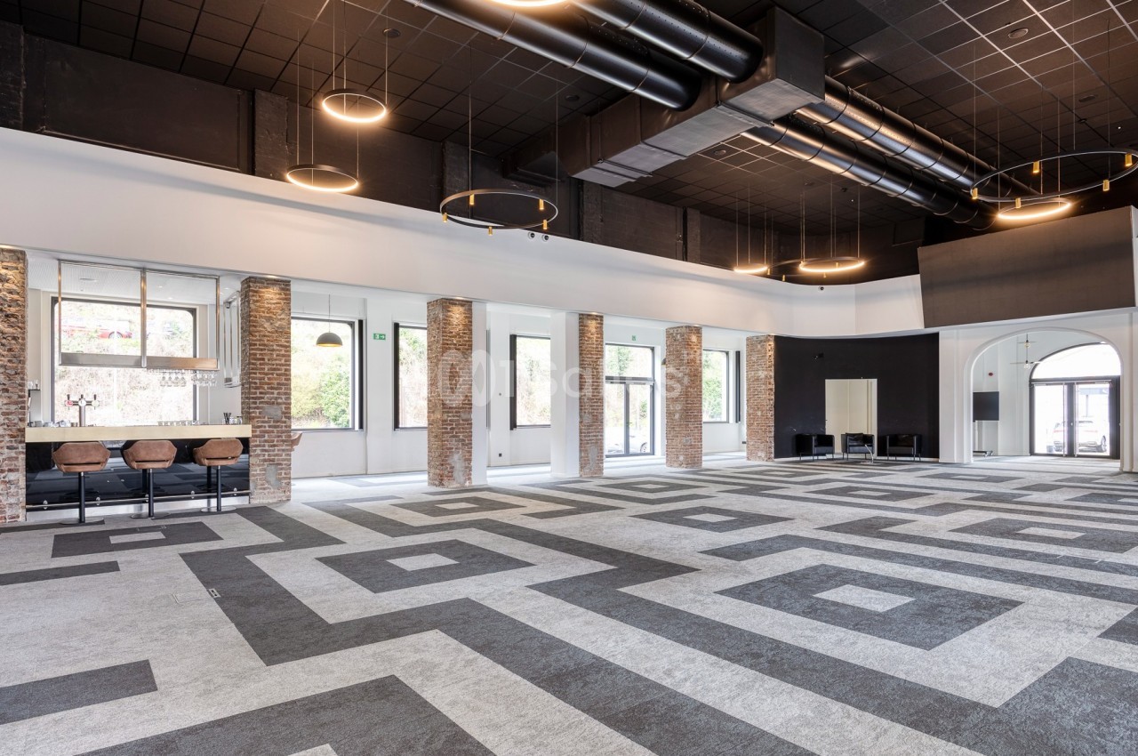 Intérieur d'une grande salle moderne avec sol géométrique, murs en briques, bar et luminaires suspendus.