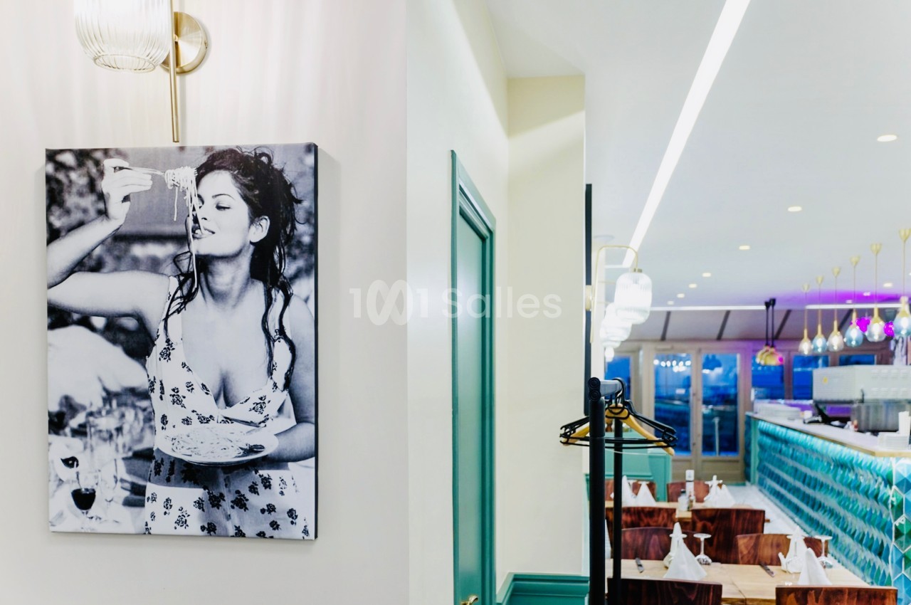 Photographie en noir et blanc d'une femme accrochée au mur d'un restaurant lumineux avec des tables et un bar.