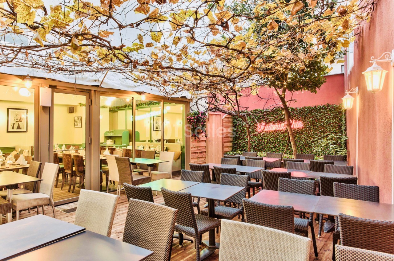 Terrasse d'un restaurant avec tables et chaises en osier, pergola couverte de vignes et éclairage chaleureux.