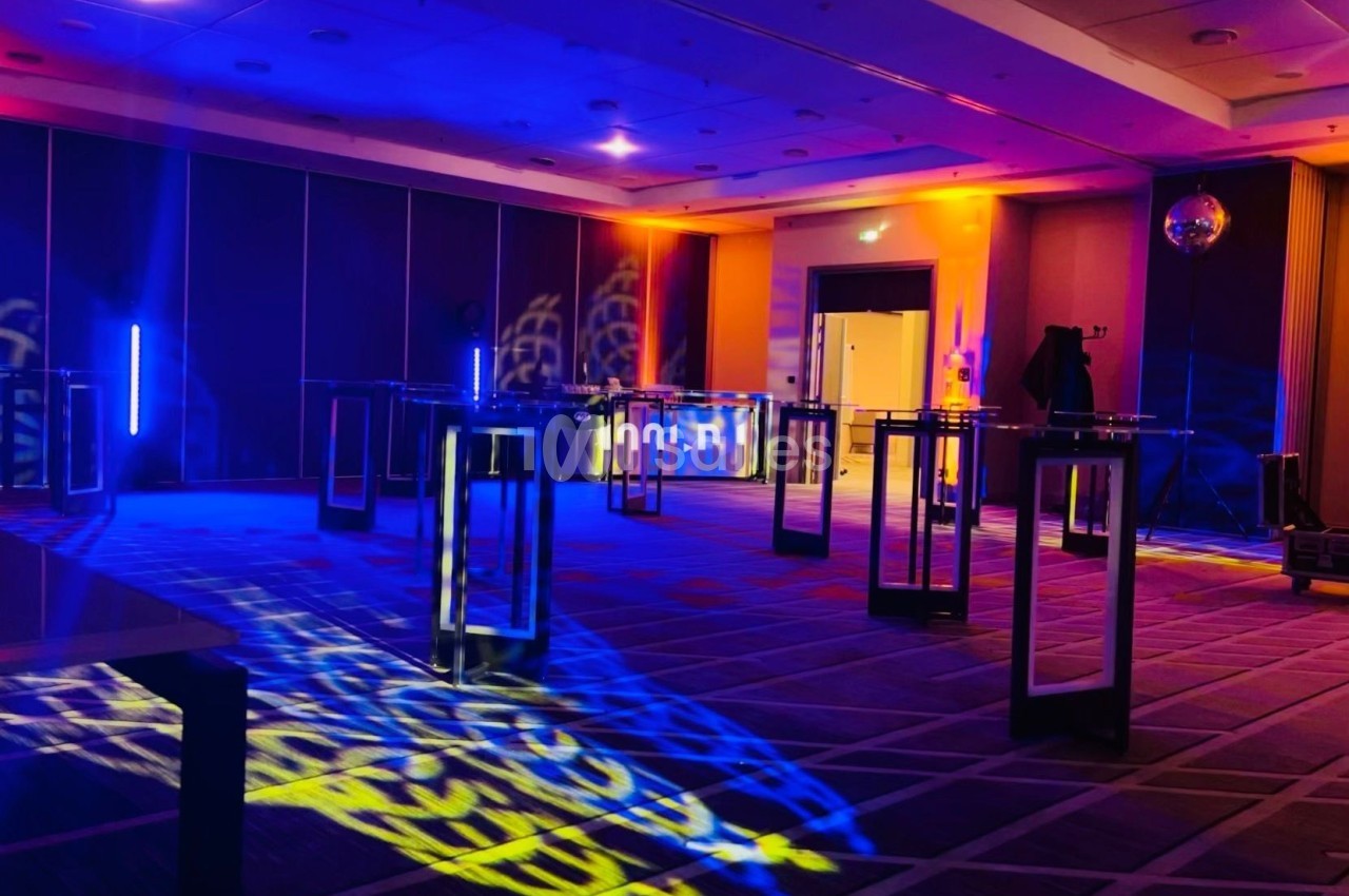 Salle de réception avec éclairage coloré, tables hautes et ambiance festive.