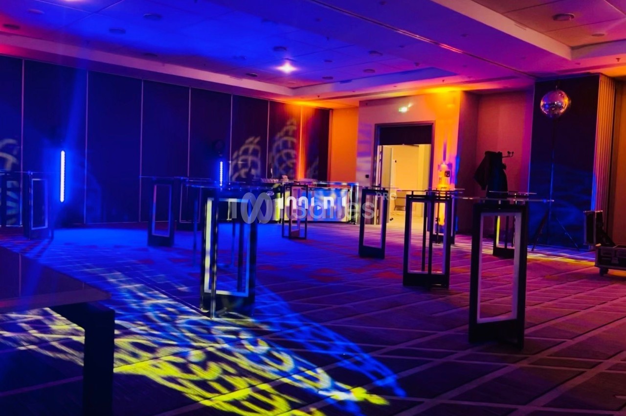 Salle de réception avec éclairage coloré, tables hautes et ambiance festive.