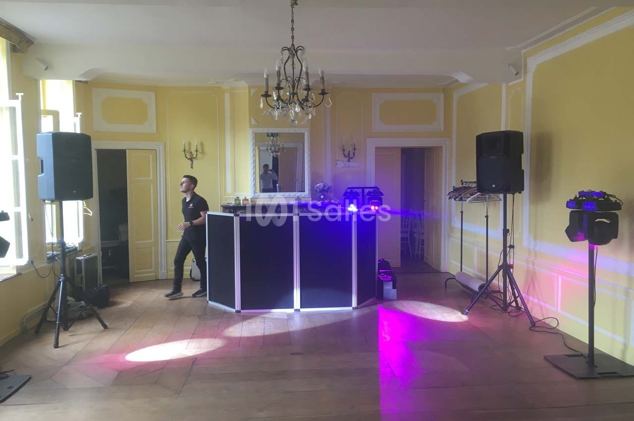 Salle lumineuse avec murs jaunes, parquet en bois, équipement de DJ installé et éclairage violet.