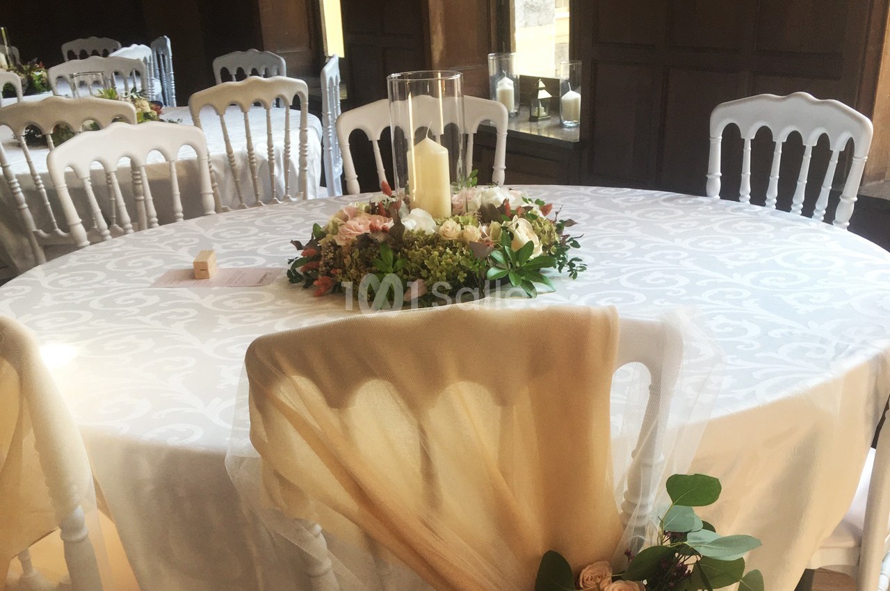 Table ronde décorée pour un événement, avec nappe blanche, centre de table floral et bougie cylindrique.